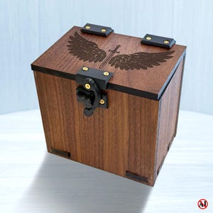May include: A square wooden box with a dark brown finish, featuring a laser-engraved design of a sword centered between two large wings on the lid. The box includes black metal hinges and a black metal latch secured with small gold-colored screws.