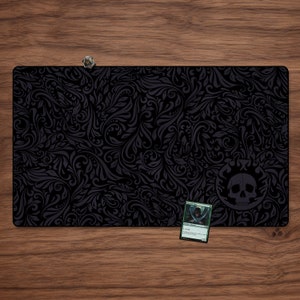 May include: Black playmat with a dark gray floral pattern and a skull design in the bottom right corner. The playmat is designed for tabletop games like Magic: The Gathering.