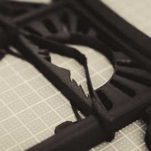 Może przedstawiać: Czarny model 3D wydrukowany w technologii 3D z geometrycznym wzorem w kształcie promieni słonecznych. Model znajduje się na szarej powierzchni siatki.