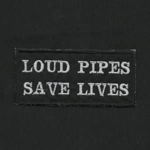 May include: Black embroidered patch with white text that reads "Loud Pipes Save Lives".