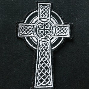May include: A black and white embroidered Celtic cross patch. The design features detailed knotwork patterns within the cross shape and a circular center. Ideal for application on clothing or accessories.