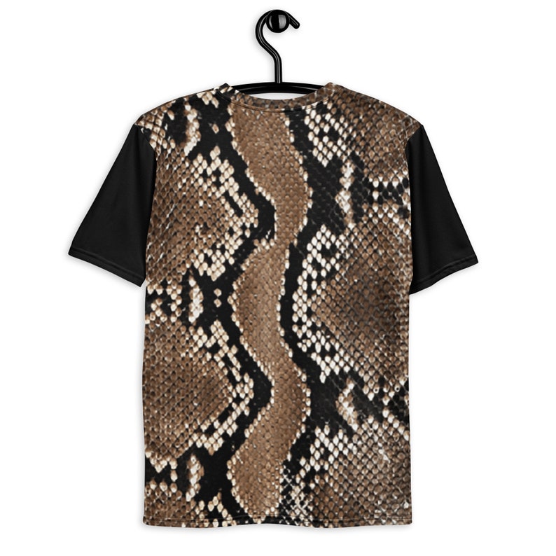 May include: A short-sleeved t-shirt with a snakeskin pattern on the front and back. The sleeves are solid black. The snakeskin design features shades of brown, tan, and black, creating a realistic reptile skin effect. The shirt is hanging on a black hanger.