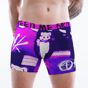 Puede incluir: Calzoncillos bóxer con un vibrante diseño púrpura y rosa. Los calzoncillos presentan un gráfico de cerdo de dibujos animados y el texto "KEEP ME SAFE". El diseño también incluye elementos gráficos y texto en blanco.