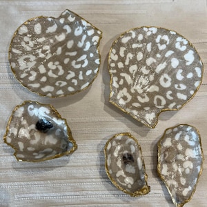 Könnte beinhalten: Fünf dekorative Muscheln mit goldener Einfassung und einem weißen und braunen Leopardenmuster.