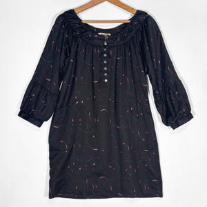 May include: Black dress with a scoop neckline and three-quarter sleeves. The dress features a button-down front and is adorned with a delicate pattern of red and white curved lines. The sleeves have a gathered, puffy design.