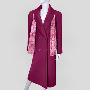 May include: A long, double-breasted magenta coat with a wide collar and decorative paisley print panels. The coat features two rows of buttons and a classic, tailored silhouette. The paisley print incorporates shades of pink and red.