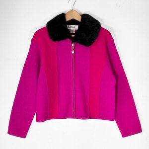 Könnte beinhalten: Eine leuchtend fuchsia- und magentafarbene, farblich abgesetzte Reißverschlussjacke mit einem kontrastierenden schwarzen Kunstfellkragen. Das Kleidungsstück hat einen goldfarbenen Reißverschlussanhänger und ein weißes Innenetikett mit dem Text Lisa am Halsausschnitt.