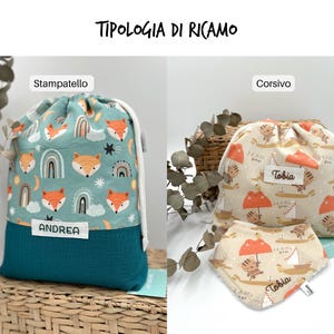 May include: Two drawstring bags and a bib. The left bag is teal with a fox and rainbow pattern and a white label reading ANDREA. The right bag and bib are beige with a tiger and sailboat pattern, featuring white labels with the name Tobia.
