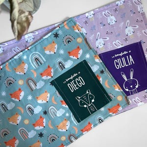 Può includere: Due coperte per bambini personalizzate. Una è verde acqua con volpi arancioni, arcobaleni e stelle. L'altra è lavanda con conigli bianchi. Ognuna ha una tasca con un nome e un'illustrazione di animali abbinata.