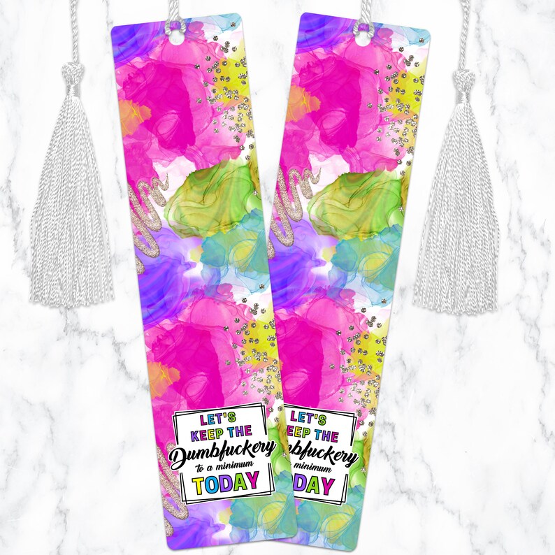 May include: Two colorful bookmarks with a white tassel. The bookmarks have a pink, green, blue, and purple abstract watercolor background with silver glitter. The text on the bookmarks reads "Let's keep the Dumbfuckery to a minimum today".