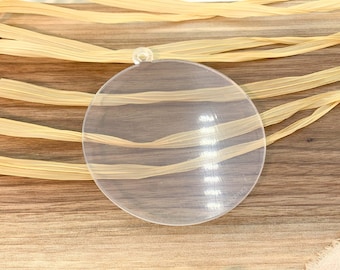 May include: A clear round plastic ornament with a hole at the top. The ornament is sitting on a wooden surface.