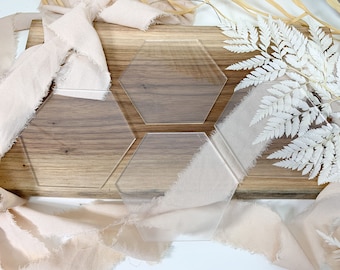 May include: Three clear acrylic hexagon-shaped coasters on a wooden surface. The coasters are arranged in a staggered pattern.
