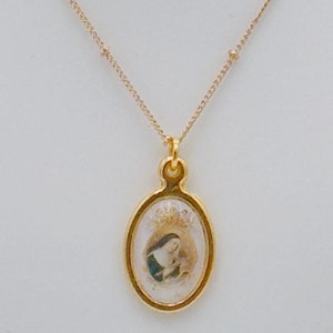 May include: Gold chain necklace with a gold oval pendant featuring a religious image of a woman in a blue robe holding a baby.