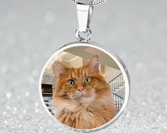 May include: A silver necklace with a round pendant featuring a close-up photo of a ginger cat with green eyes. The cat is looking directly at the camera.
