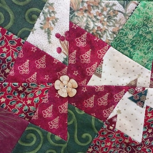 K&ouml;nnte beinhalten: Nahaufnahme einer roten, gr&uuml;nen und wei&szlig;en Patchwork-Decke mit einem Holzknopf in der Mitte. Die Decke besteht aus verschiedenen Stoffen mit unterschiedlichen Mustern, darunter Sterne, B&auml;ume und Spiralen.