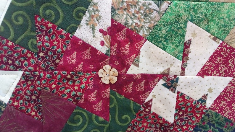 K&ouml;nnte beinhalten: Nahaufnahme einer roten, gr&uuml;nen und wei&szlig;en Patchwork-Decke mit einem Holzknopf in der Mitte. Die Decke besteht aus verschiedenen Stoffen mit unterschiedlichen Mustern, darunter Sterne, B&auml;ume und Spiralen.