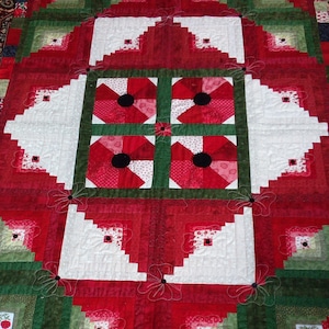 May include: A red, white, and green quilt with a log cabin pattern and a central design of four red flowers with black centers.