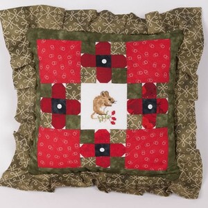 Może przedstawiać: Poduszka w patchworku zielonym i czerwonym z wyszytym w środku myszką i kwiatami. Poduszka ma falbankę.