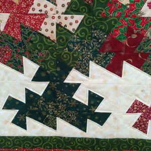 K&ouml;nnte beinhalten: Eine Nahaufnahme einer Weihnachtsdecke mit wei&szlig;em Hintergrund und einem Muster aus gr&uuml;nen und roten Dreiecken. Die Decke besteht aus verschiedenen Stoffen mit verschiedenen Mustern, darunter Schneeflocken, Stechpalmen und Spiralen.