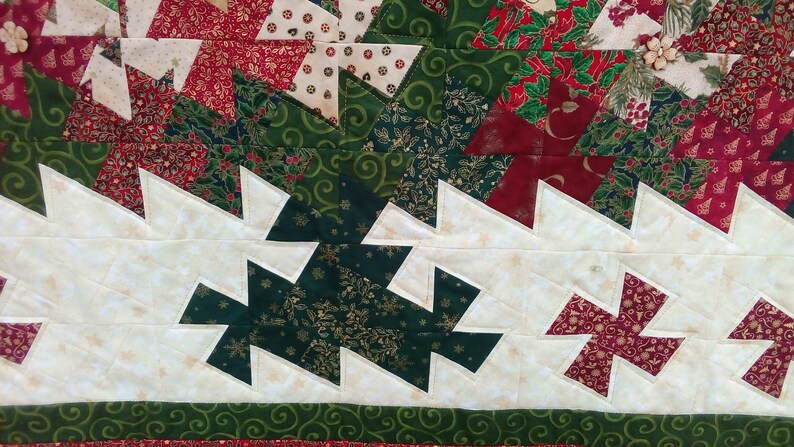 K&ouml;nnte beinhalten: Eine Nahaufnahme einer Weihnachtsdecke mit wei&szlig;em Hintergrund und einem Muster aus gr&uuml;nen und roten Dreiecken. Die Decke besteht aus verschiedenen Stoffen mit verschiedenen Mustern, darunter Schneeflocken, Stechpalmen und Spiralen.