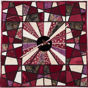 Peut inclure: Une courtepointe en patchwork rouge, blanc et violet avec un cadran d'horloge au centre. Le cadran d'horloge est entouré d'un cercle noir avec un ruban rouge et une petite fleur.