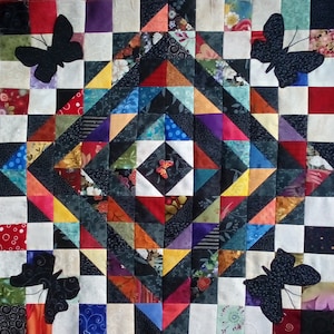 Könnte beinhalten: Ein farbenfroher Quilt mit einem geometrischen Muster aus schwarzen Dreiecken und Quadraten. Der Quilt hat eine zentrale Diamantform mit einem kleineren Diamanten in der Mitte. Der Quilt ist mit schwarzen Schmetterlingsapplikationen verziert.