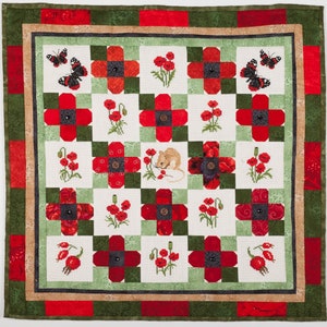May include: A square quilt with a patchwork design featuring red poppies, butterflies, and a mouse. The quilt has a green and red border, with a beige inner border. The central design is a grid of squares with embroidered details.
