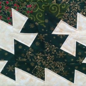 K&ouml;nnte beinhalten: Ein Patchwork-Quiltblock mit Weihnachtsmotiv. Der Block besteht aus wei&szlig;em, gr&uuml;nem und goldenem Stoff. Der gr&uuml;ne Stoff hat ein Muster aus Stechpalmenbl&auml;ttern und Schneeflocken. Der wei&szlig;e Stoff hat eine subtile Textur. Der Block ist in einem Zickzackmuster zusammengen&auml;ht.