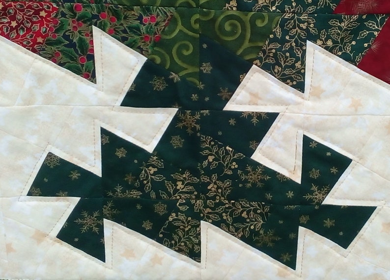 K&ouml;nnte beinhalten: Ein Patchwork-Quiltblock mit Weihnachtsmotiv. Der Block besteht aus wei&szlig;em, gr&uuml;nem und goldenem Stoff. Der gr&uuml;ne Stoff hat ein Muster aus Stechpalmenbl&auml;ttern und Schneeflocken. Der wei&szlig;e Stoff hat eine subtile Textur. Der Block ist in einem Zickzackmuster zusammengen&auml;ht.