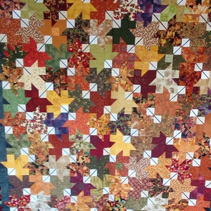 May include: A patchwork quilt with a variety of autumnal colours, including red, orange, yellow, brown and green. The quilt is made up of small squares and triangles, and the design is reminiscent of autumn leaves.