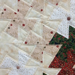 K&ouml;nnte beinhalten: Ein Patchwork-Deckenst&uuml;ck mit einer Vielzahl von Stoffen in Gr&uuml;n-, Rot-, Wei&szlig;- und Braunt&ouml;nen. Die Decke besteht aus Dreiecken und Quadraten und zeigt verschiedene Muster, darunter Punkte, florale Designs und geometrische Formen.