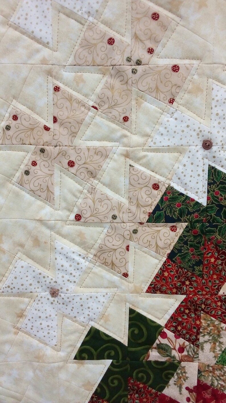 K&ouml;nnte beinhalten: Ein Patchwork-Deckenst&uuml;ck mit einer Vielzahl von Stoffen in Gr&uuml;n-, Rot-, Wei&szlig;- und Braunt&ouml;nen. Die Decke besteht aus Dreiecken und Quadraten und zeigt verschiedene Muster, darunter Punkte, florale Designs und geometrische Formen.