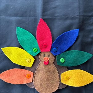 May include: A felt turkey craft with a brown body and colorful felt feathers. The feathers are attached with buttons in various colors, including red, green, blue, yellow, and orange.