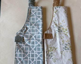 May include: Two hanging kitchen towels with fabric loops. The left towel features a blue and white geometric lattice pattern. The right towel has a white background with a green and grey leaf print. Both have matching solid color fabric tabs.
