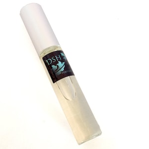 Puede incluir: Una botella de vidrio transparente con una tapa blanca y una etiqueta marrón que dice "DSH PERFUME".