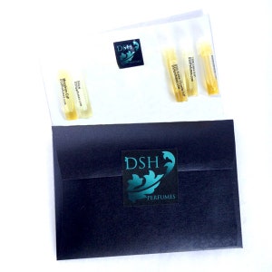 May include: A black envelope with a teal logo that says "DSH Perfumes" on the front. The envelope contains small glass vials of perfume with labels that say "DSH Perfumes" and "DSH Perfumes.com".