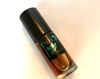 May include: A small, clear glass bottle with a black cap and a brown liquid inside. The bottle has a label with the text "DSH PERFUMES" in a teal blue font.