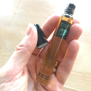 May include: A small, clear glass bottle with a black rollerball top. The bottle contains a light brown liquid. The bottle is labeled "Samarkand" and "DSH Perfumes".