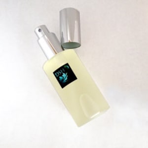Könnte beinhalten: Eine durchsichtige Glasflasche mit einem silbernen Sprühkopf und Verschluss. Die Flasche hat ein schwarzes Etikett mit dem Text "DSH" und einem stilisierten Blattdesign.