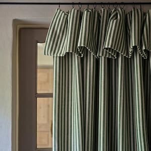May include: A floor-length curtain featuring a vertical striped pattern in dark forest green and off-white. The fabric is gathered at the top with metal rings attached to a black horizontal rod, creating deep, uniform folds along the length.