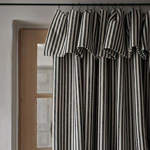 May include: Black and white striped curtains hanging from a dark metal rod. The curtains are made of a textured fabric and are partially covering a wooden door and window. The stripes are vertical and evenly spaced.