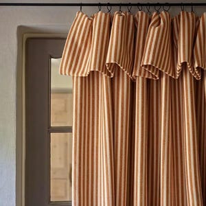 May include: Brown and cream striped curtains hanging from a black rod above a window. The vertical stripes create a classic, farmhouse style. The curtains are made of a thick fabric.
