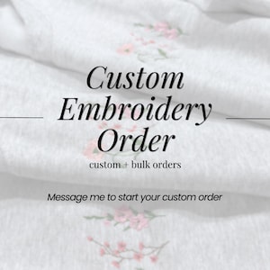May include: White fabric with the text "Custom Embroidery Order" in a stylish font. The text "custom + bulk orders" is below the main text. Pink floral embroidery accents the fabric. The phrase "Message me to start your custom order" is also included.