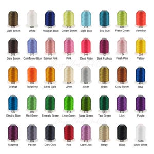 May include: A color chart of embroidery thread spools in various colors, including light brown, white, Prussian blue, cream brown, and light blue. Each spool is labeled with a color name and number. The chart includes a wide range of colors.