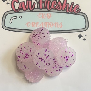 May include: A group of 8 small, round, translucent, white car air fresheners with purple glitter. The air fresheners are shaped like a small, flat circle. The air fresheners are arranged in a cluster.