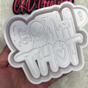 May include: A white plastic mold with the words "GOTH THOT" in a dripping font, featuring a skull and heart. The mold is held in a hand, with a black and pink "CKD Creations" logo in the background.