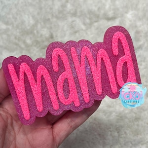 May include: A pink glittery "mama" word art design. The word "mama" is in a bubble letter style with a glittery pink outline. The background is a darker pink with glitter. The design has a rounded edge. A small logo is visible in the bottom right corner.