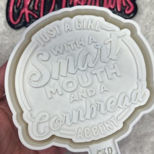 May include: White silicone mold with the text "Just a girl with a smart mouth and a cornbread accent" in a circle. The mold is for making a cake or cookie.
