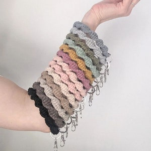 May include: A stack of 15 colorful crocheted keychains with silver key rings. The keychains are made of cotton rope and are in various shades of pink, beige, brown, green, and gray.