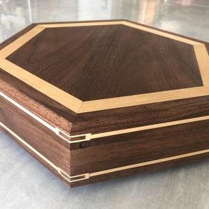 May include: Octagonal wooden box with a dark brown walnut finish and a light wood inlay. The box has a hinged lid and a decorative brass accent.